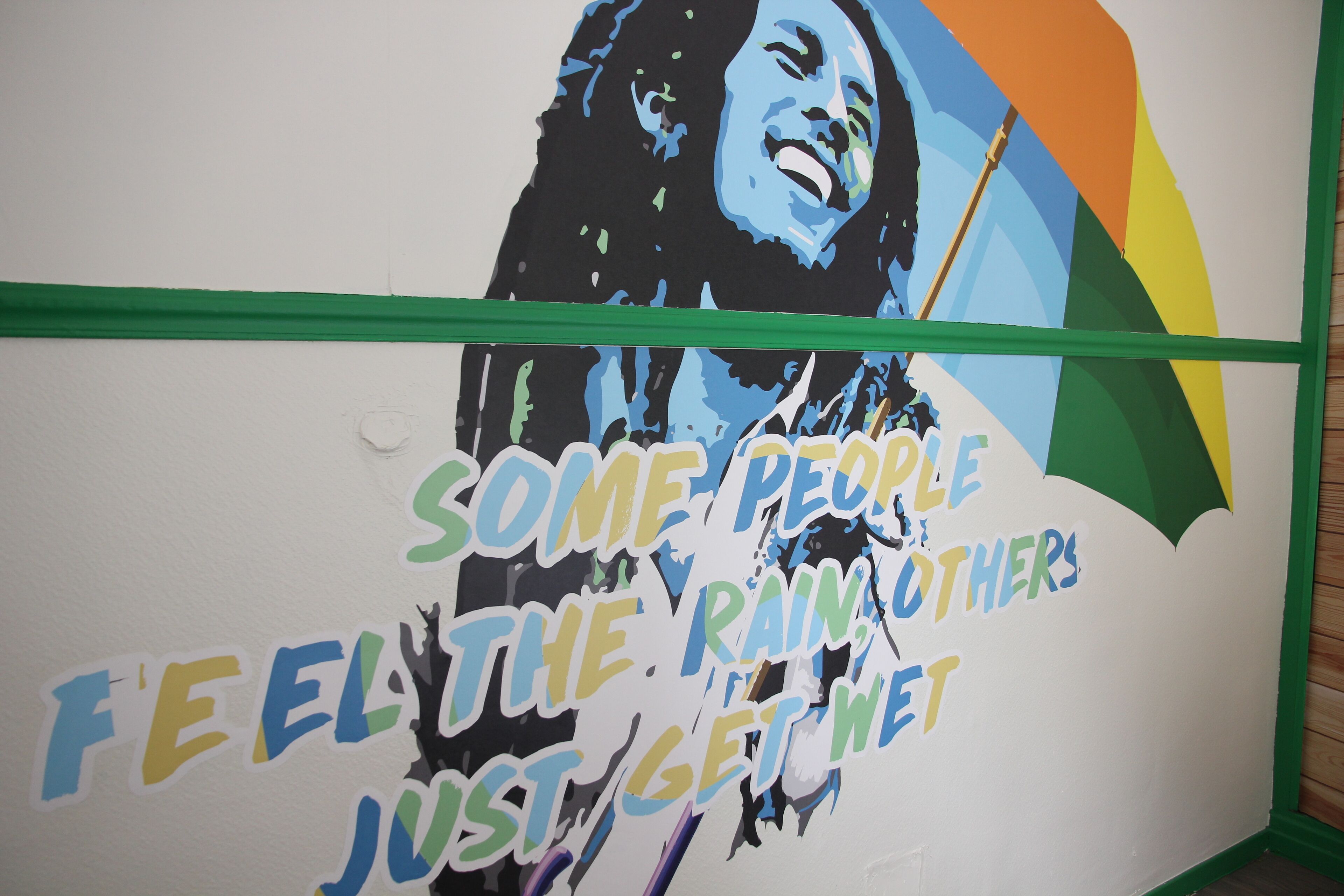 A wall with a colorful mural and the text "SOME PEOPLE FEEL THE RAIN, OTHERS JUST GET WET."