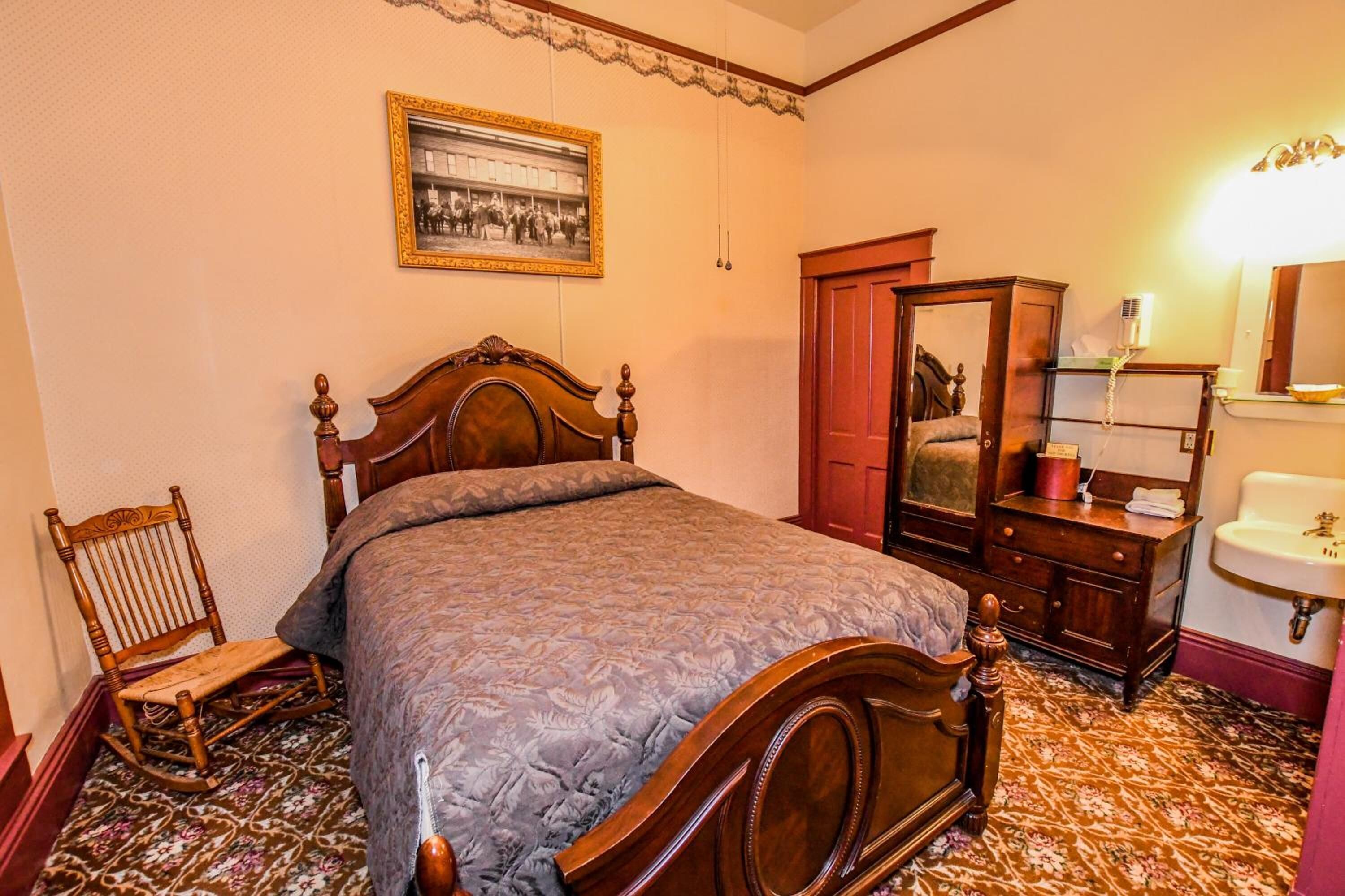 A bedroom with a wooden bed, a rocking chair, a wardrobe, a mirror, and a sink.
