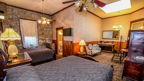 Quarto com duas camas, uma escrivaninha de madeira, uma cadeira, um espelho e um ventilador de teto.