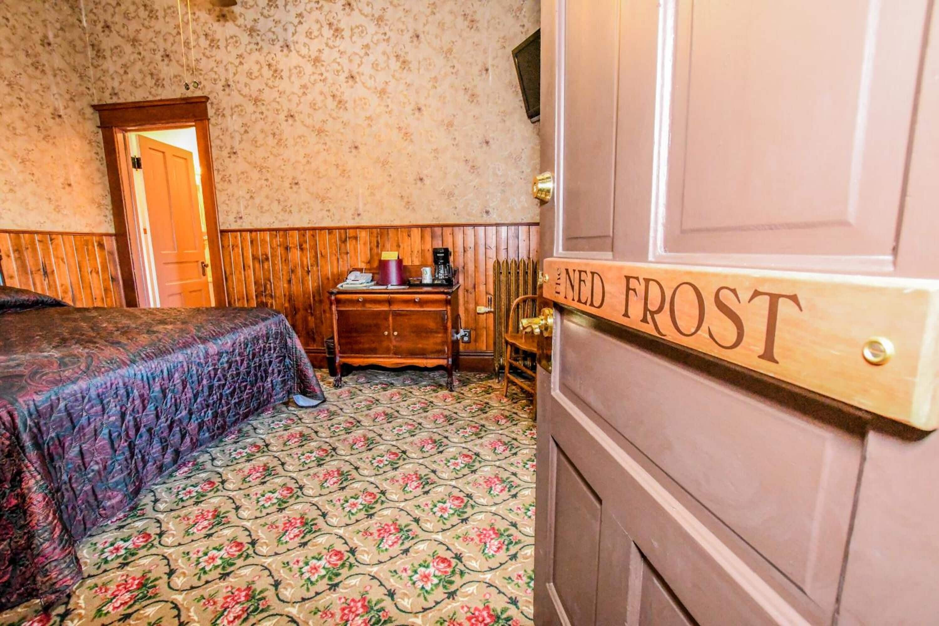 A room with a bed, a wooden dresser, a radiator, and a door labeled "NED FROST".