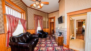 Quarto com piso de madeira, tapete estampado, sofá de couro, armário de madeira e ventilador de teto.