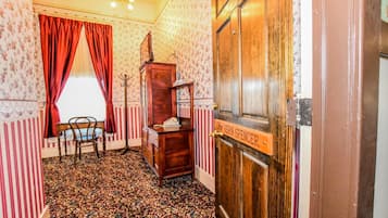 A room with striped wallpaper, a patterned carpet, a wooden desk, a chair, a coat rack, and a door labeled "The Vern Spencer".