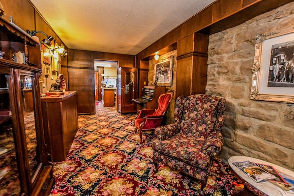Una habitación con alfombra estampada, un sillón rojo, un piano y una pared de piedra con un cuadro enmarcado.