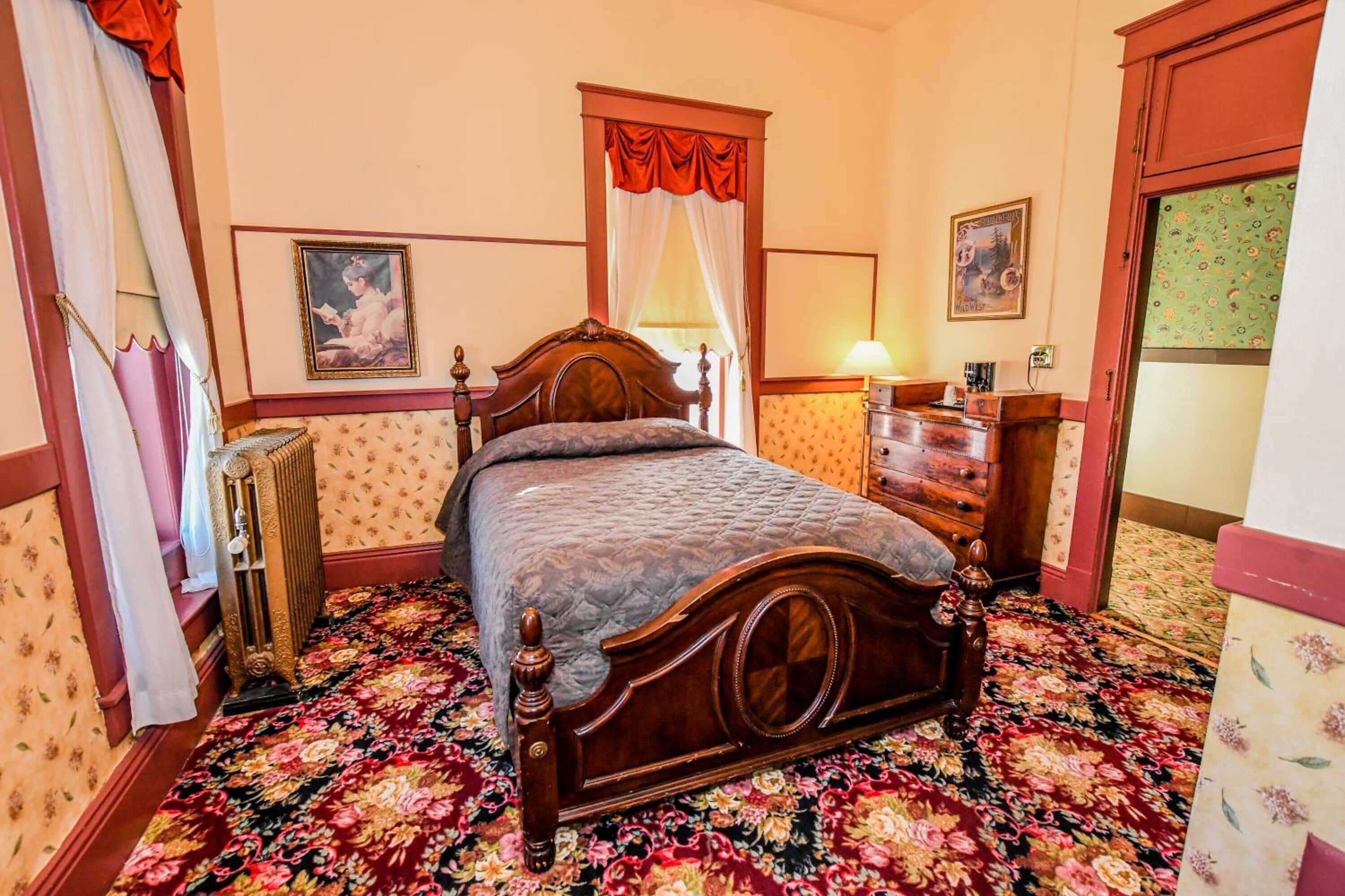 A bedroom with a wooden bed, a dresser, a radiator, and a floral carpet.