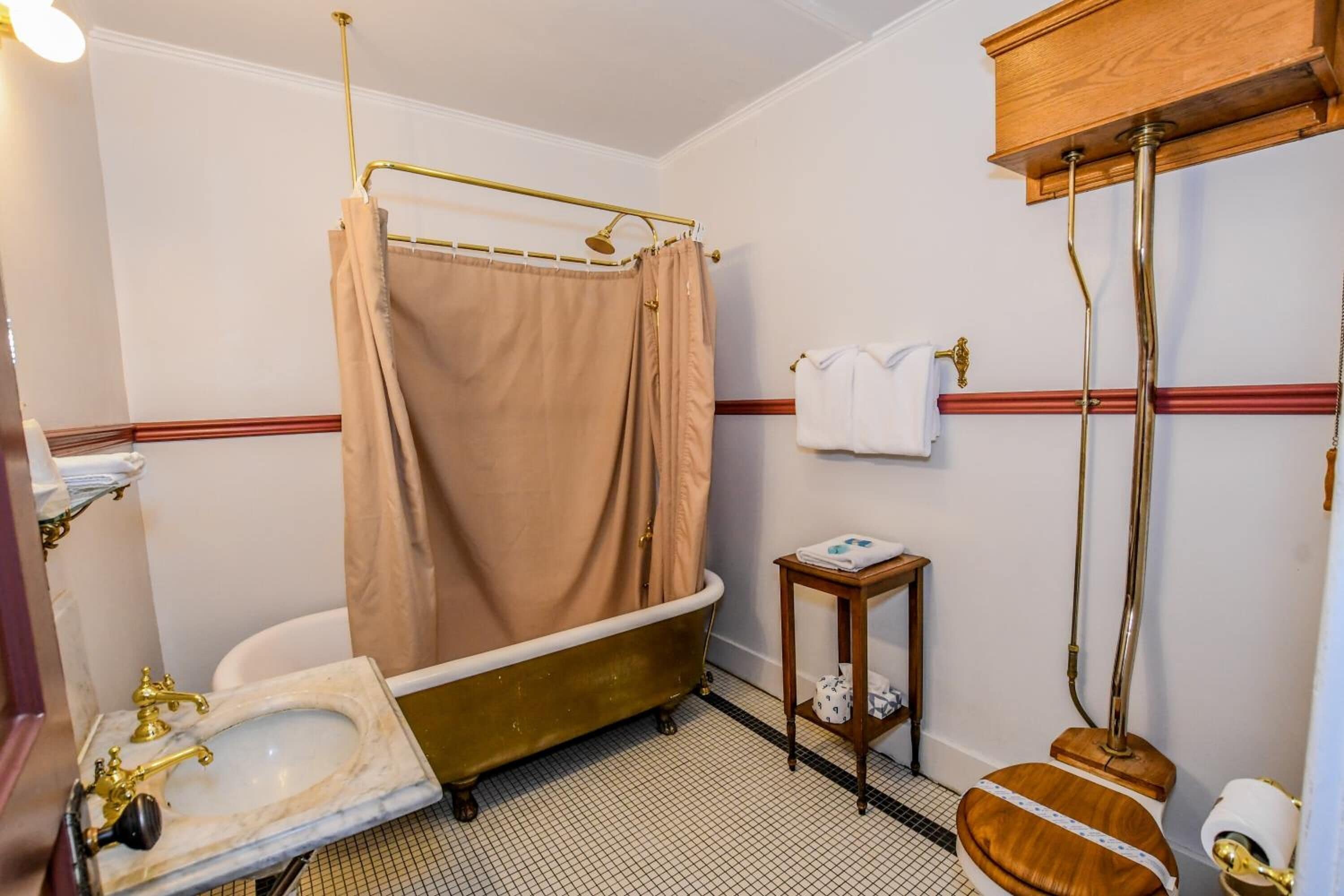 Un baño con una bañera tipo patas de león antigua, un lavamanos pedestal y un inodoro con asiento de madera.