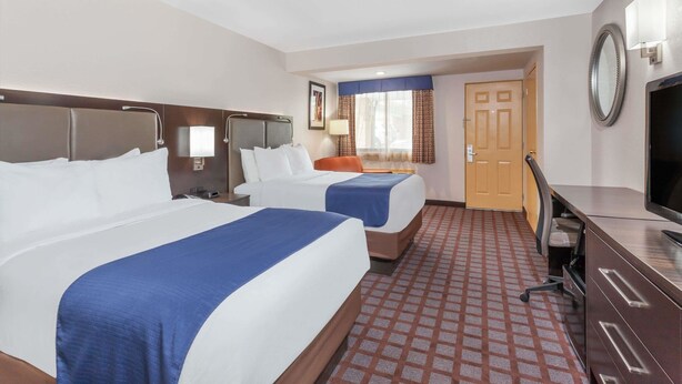 A hotel room with two beds, a desk, a television, and a door leading to another room. - Days Inn by Wyndham Woodbury Long Island (Woodbury)