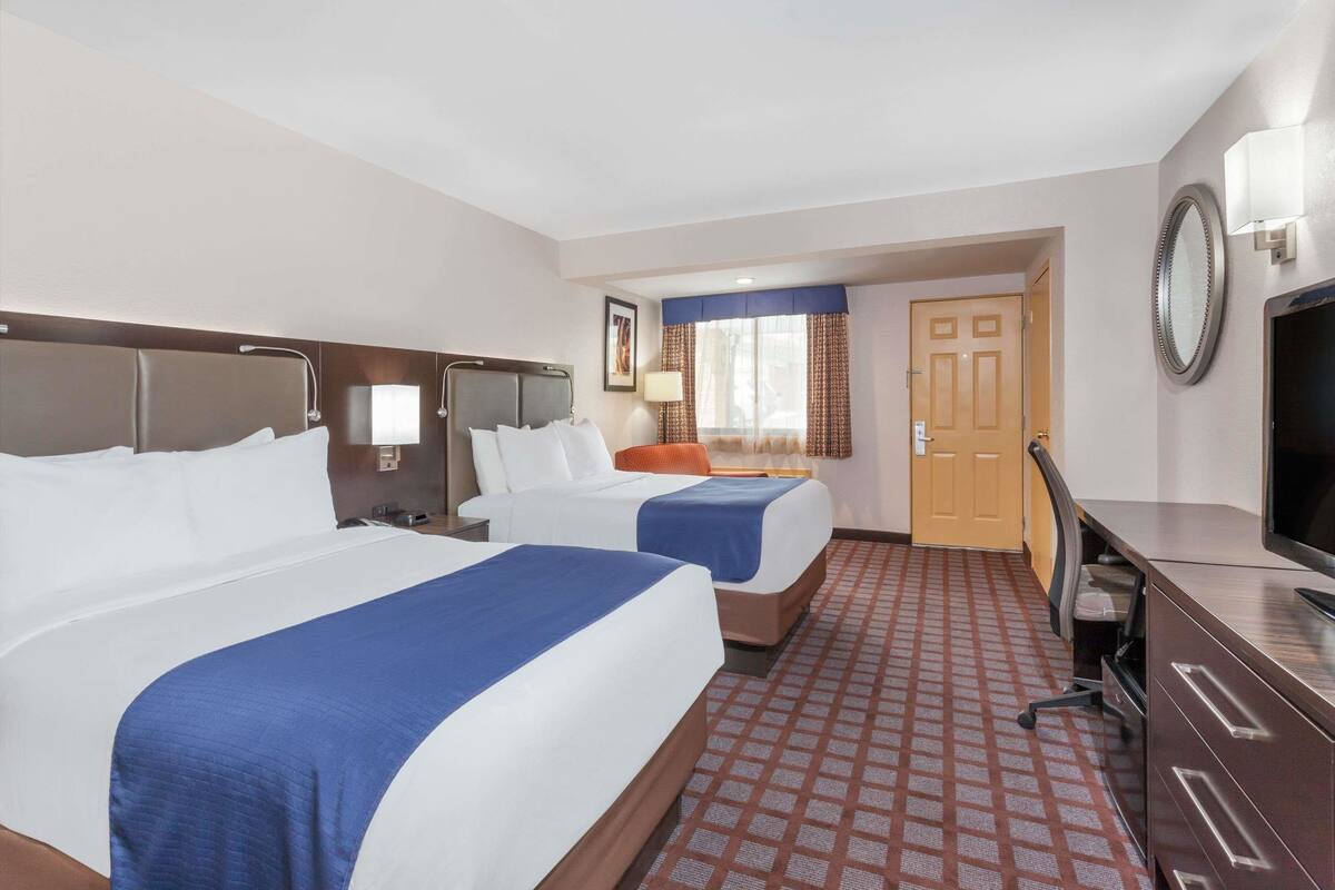 Una habitación de hotel con dos camas, un escritorio, un televisor y una puerta que da a otra habitación.