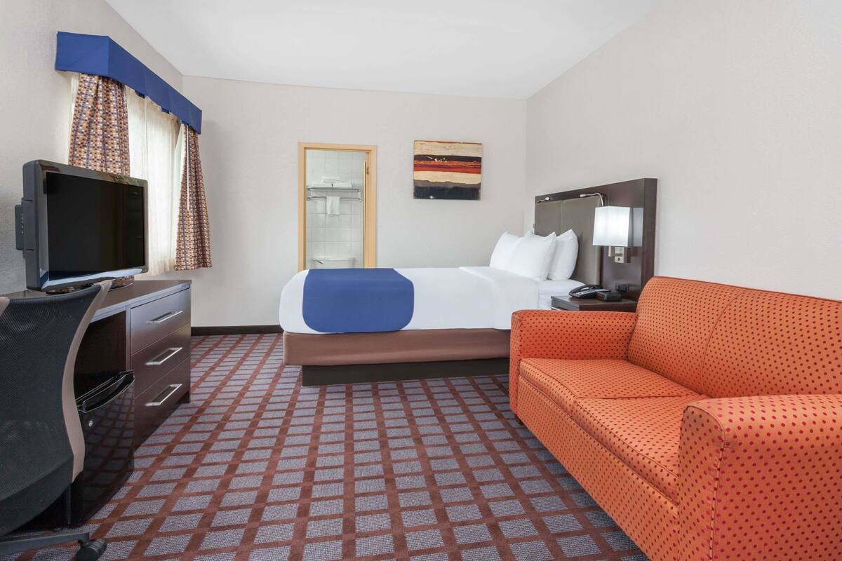Habitación de hotel con cama, escritorio con ordenador, televisor, sofá y puerta al baño.