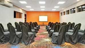 A conference room with rows of chairs, a projector screen, and a carpet with a starburst pattern. - Days Inn by Wyndham Woodbury Long Island (Woodbury)