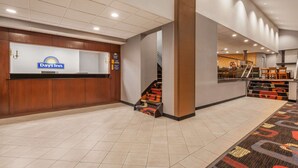 A Days Inn reception area with a reception desk, a staircase, and a carpeted floor. - Days Inn by Wyndham Woodbury Long Island (Woodbury)
