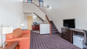 A hotel room with a staircase, a sofa, a desk with a TV, and a refrigerator. - Days Inn by Wyndham Woodbury Long Island (Woodbury)