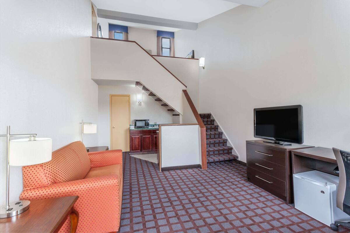 Habitación de hotel con escalera, un sofá, un escritorio con televisor y un refrigerador.