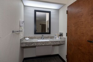 A bathroom with a granite countertop, a white sink, a mirror, and a wooden door.