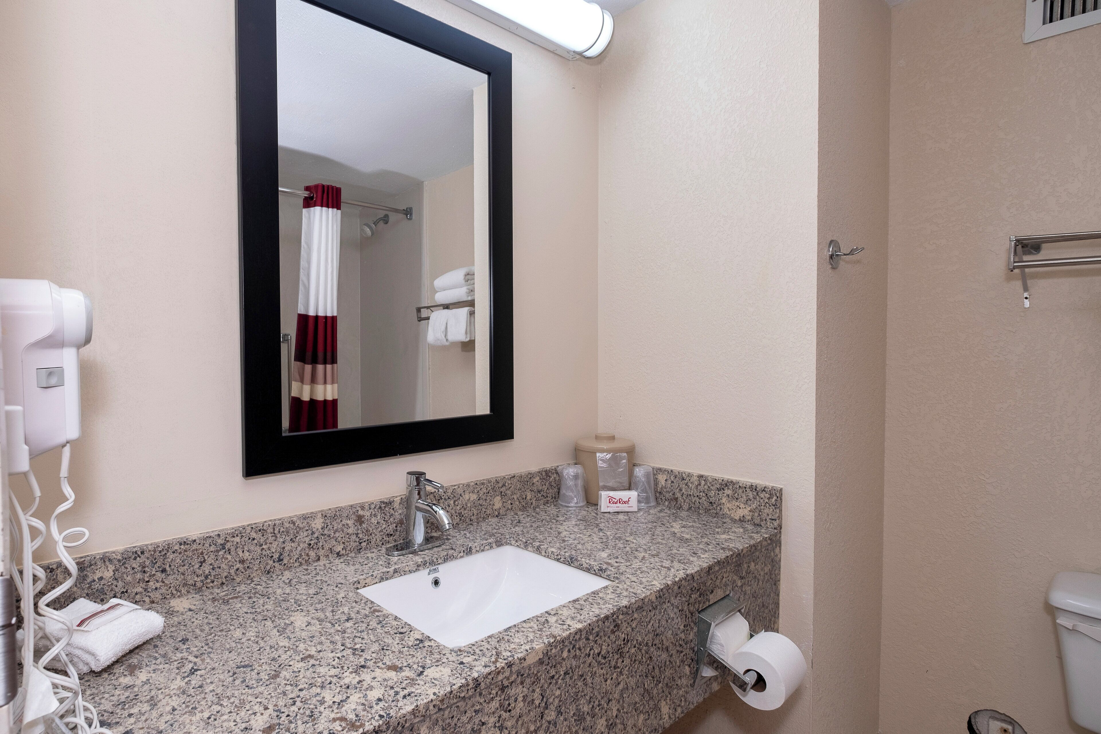 Une salle de bain dotée d’un comptoir en granit, d’un lavabo, d’un miroir, d’un porte-serviettes, d’un sèche-cheveux et d’un support à papier toilette.
