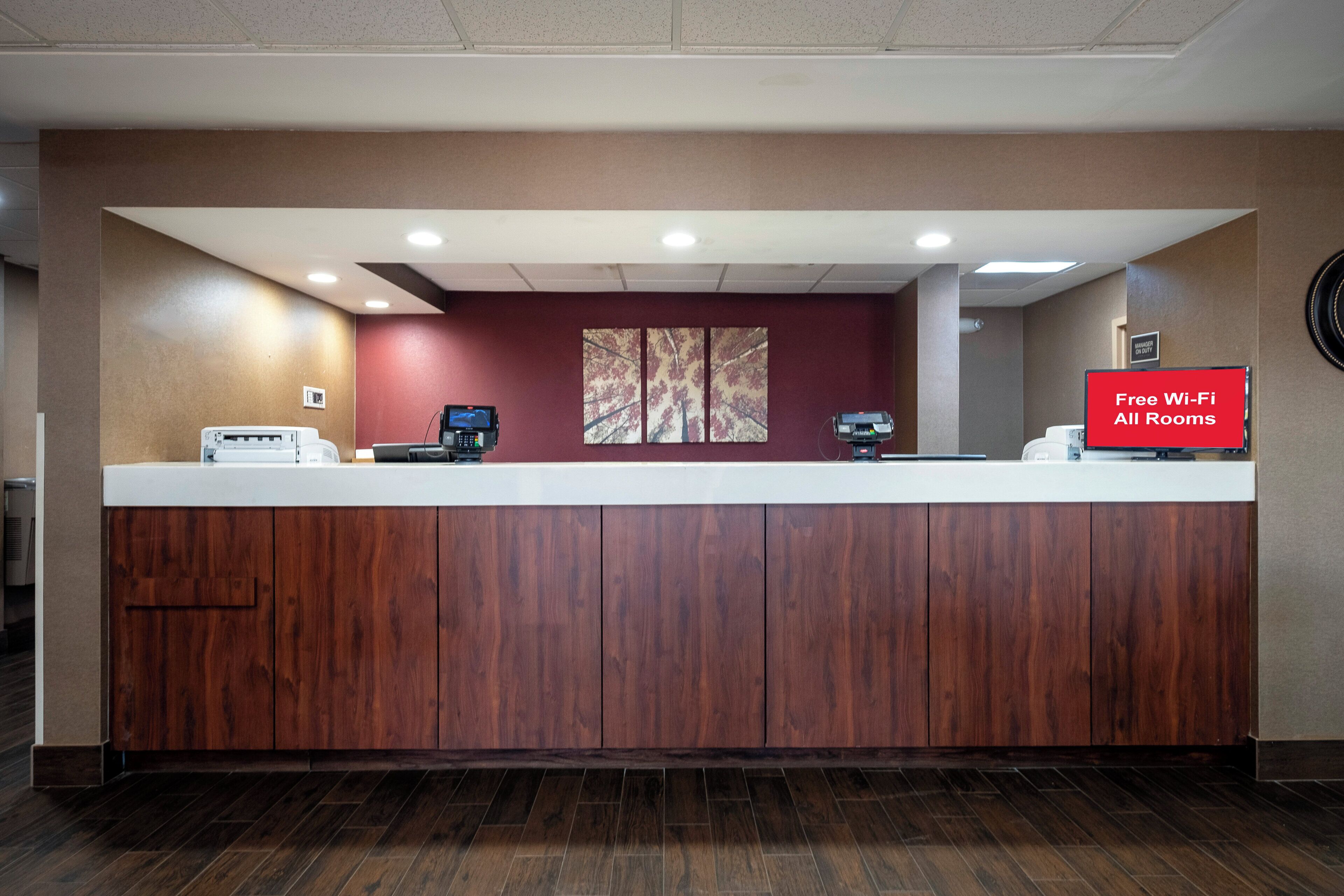 A reception desk with a digital screen, a 'Free Wi-Fi All Rooms' sign, and a 'Manager On Duty' sign.
