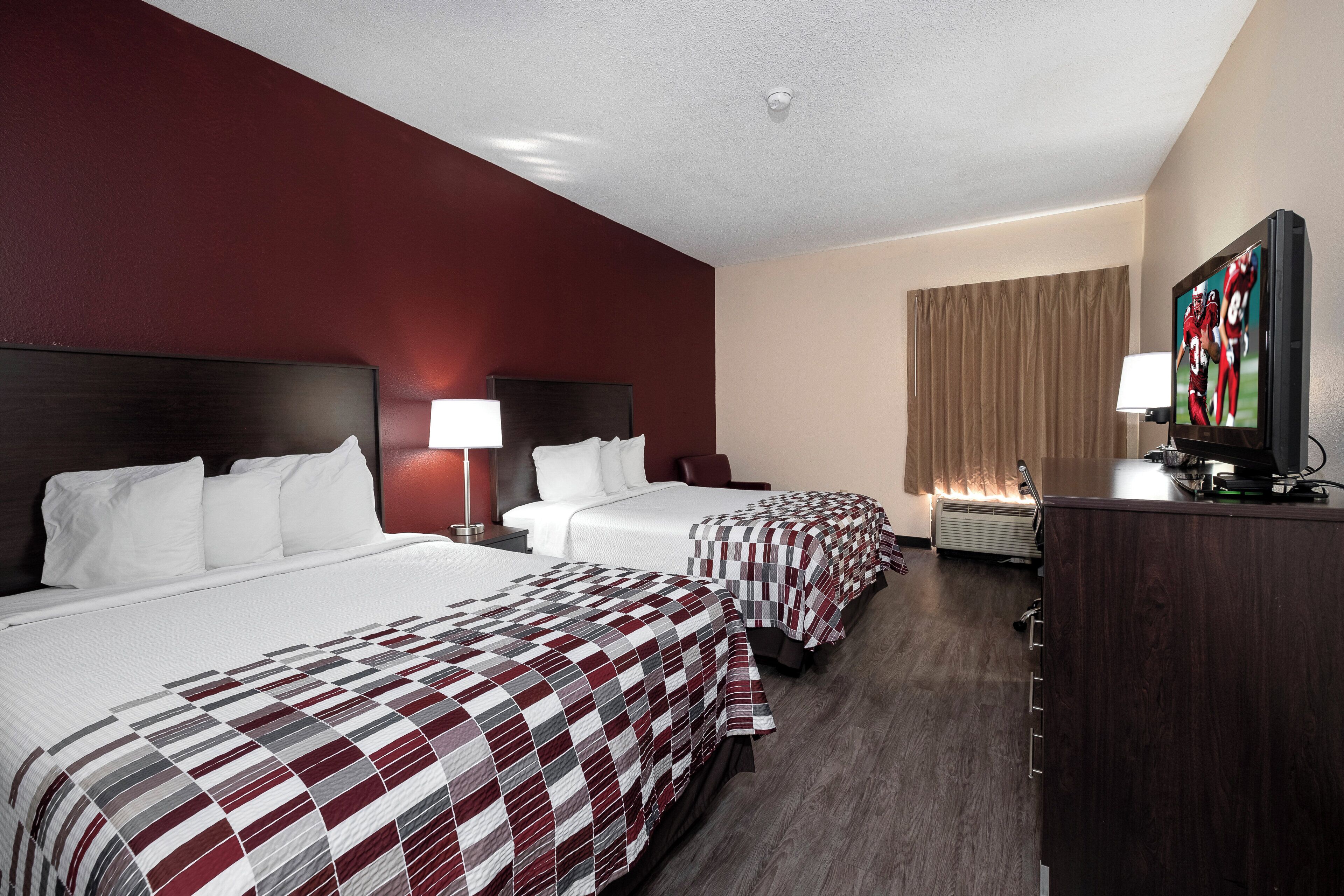 A hotel room with two beds, a television, and a desk.