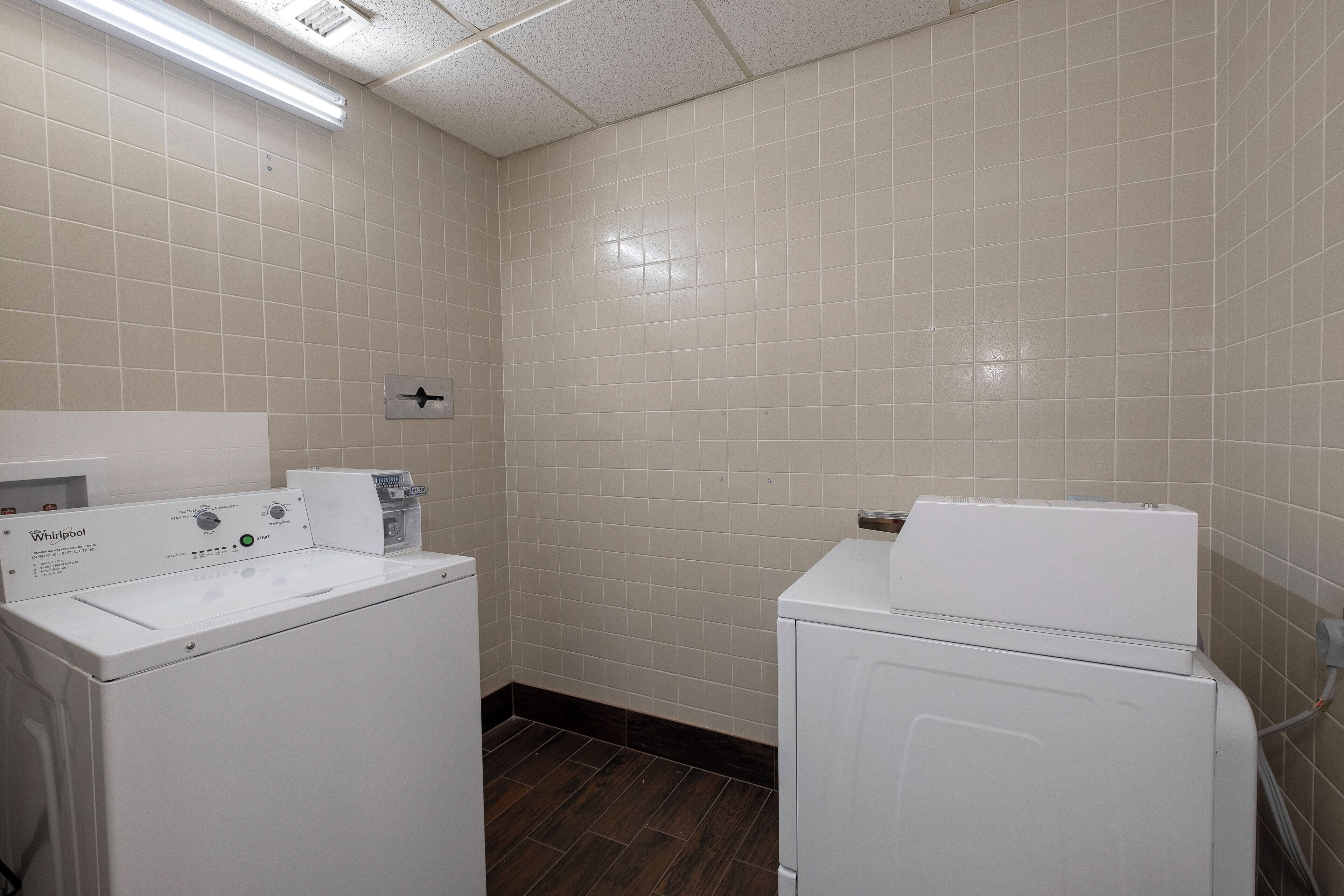 A laundry room with two Whirlpool washers, a control panel, and a tiled wall.