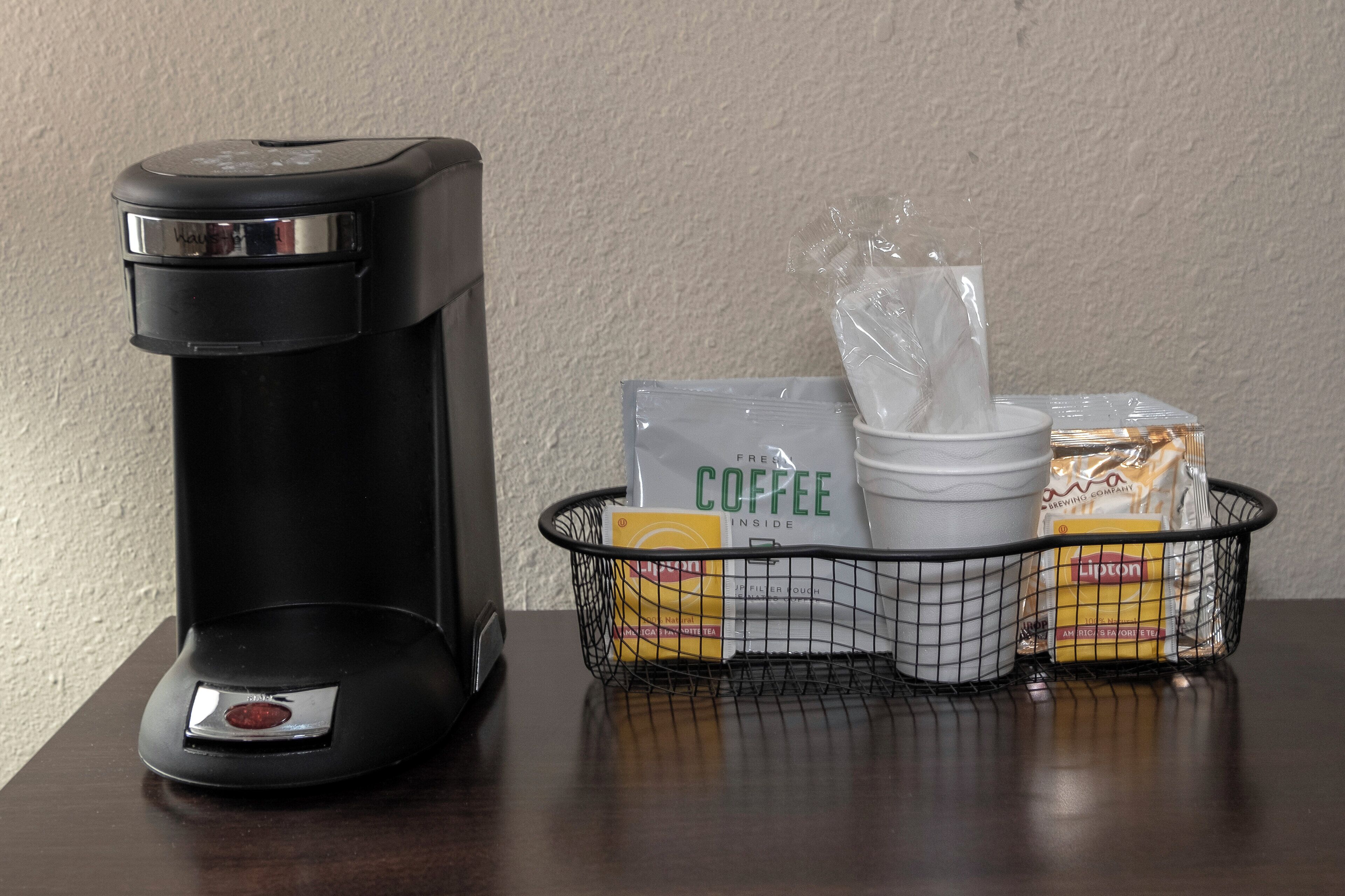 Eine Kaffeemaschine und ein Korb mit Kaffeekapseln, einer Kaffeetasse und Zucker.
