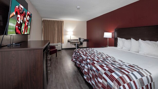 A hotel room with a bed, a desk, a television, and a window with curtains.