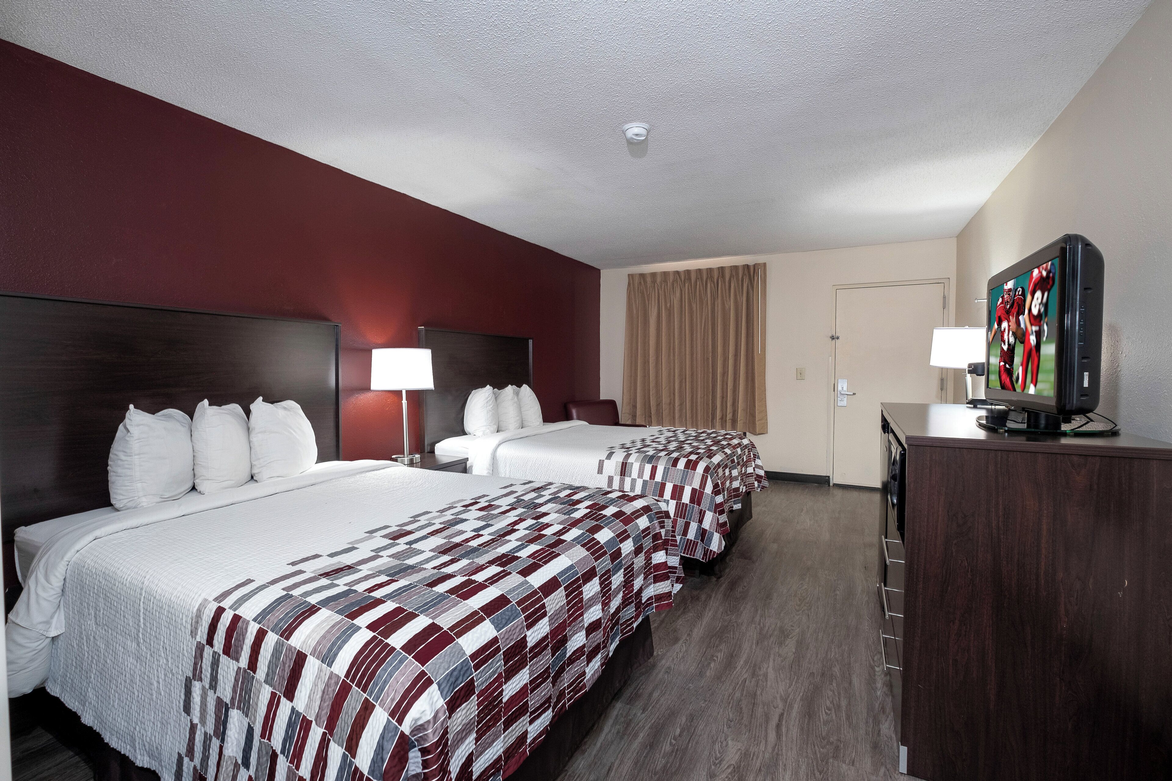 Habitación de hotel con tres camas, televisión y cómoda.