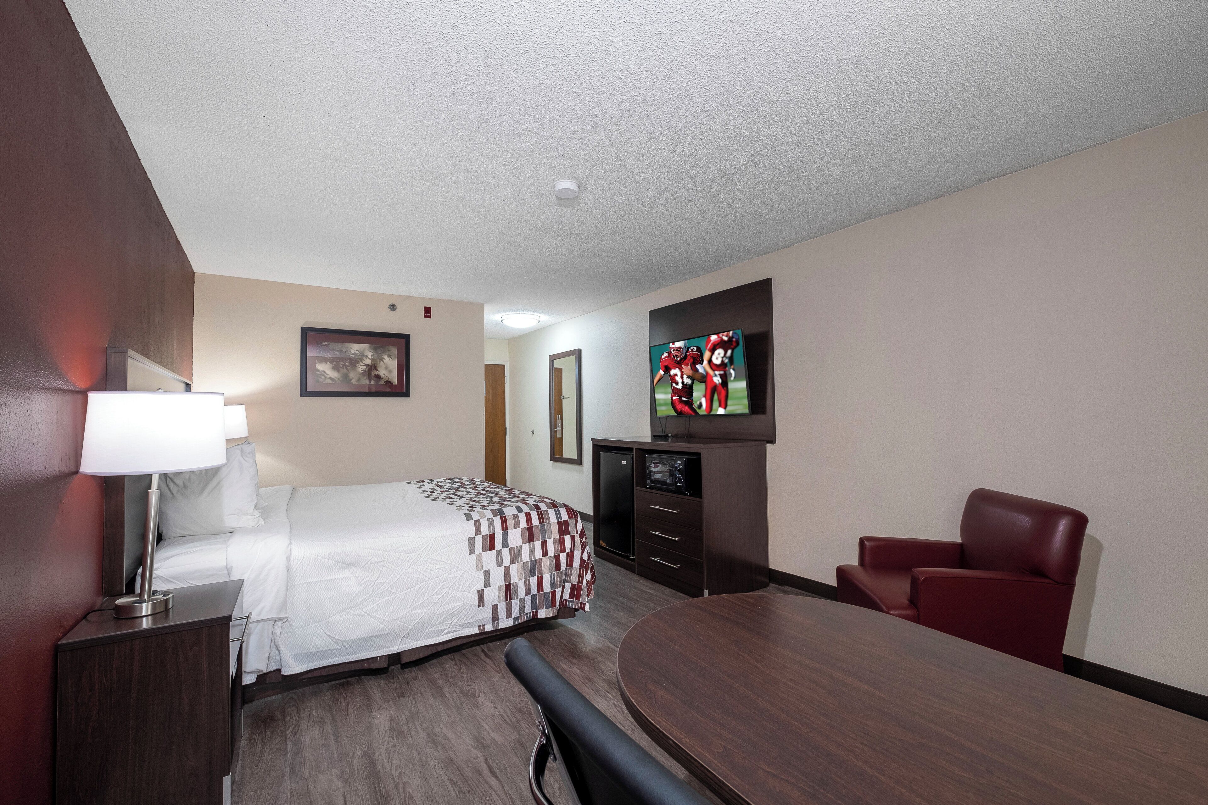 A hotel room with a bed, a desk, a chair, a TV, and a small cabinet.