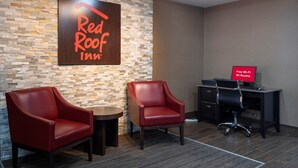 Un vestíbulo de Red Roof Inn con dos sillones de cuero, una pequeña mesa redonda, un escritorio con una computadora y un letrero que indica Wi-Fi gratis en todas las habitaciones.