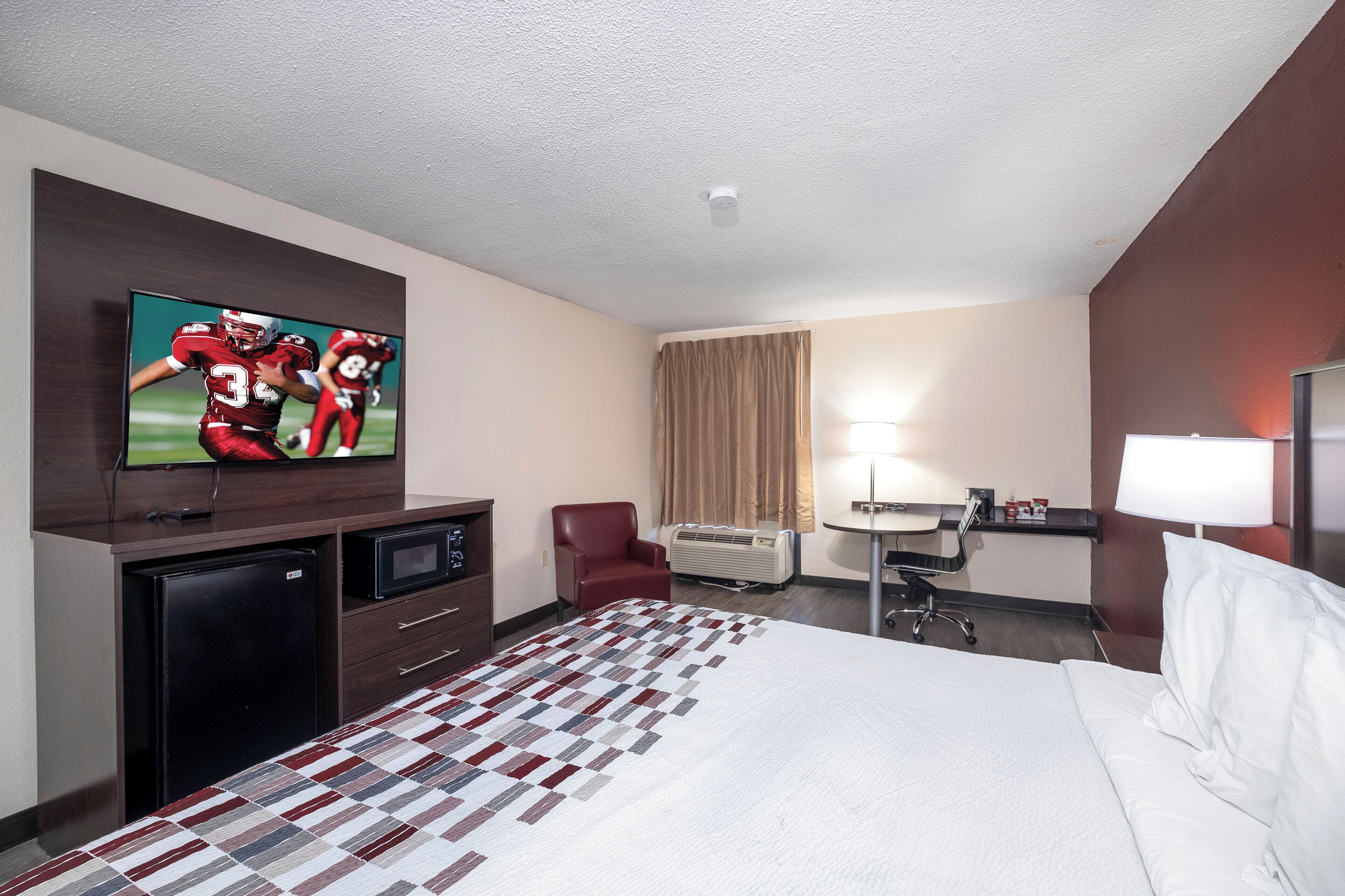 Habitación de hotel con cama, escritorio, silla, televisor y minibar.