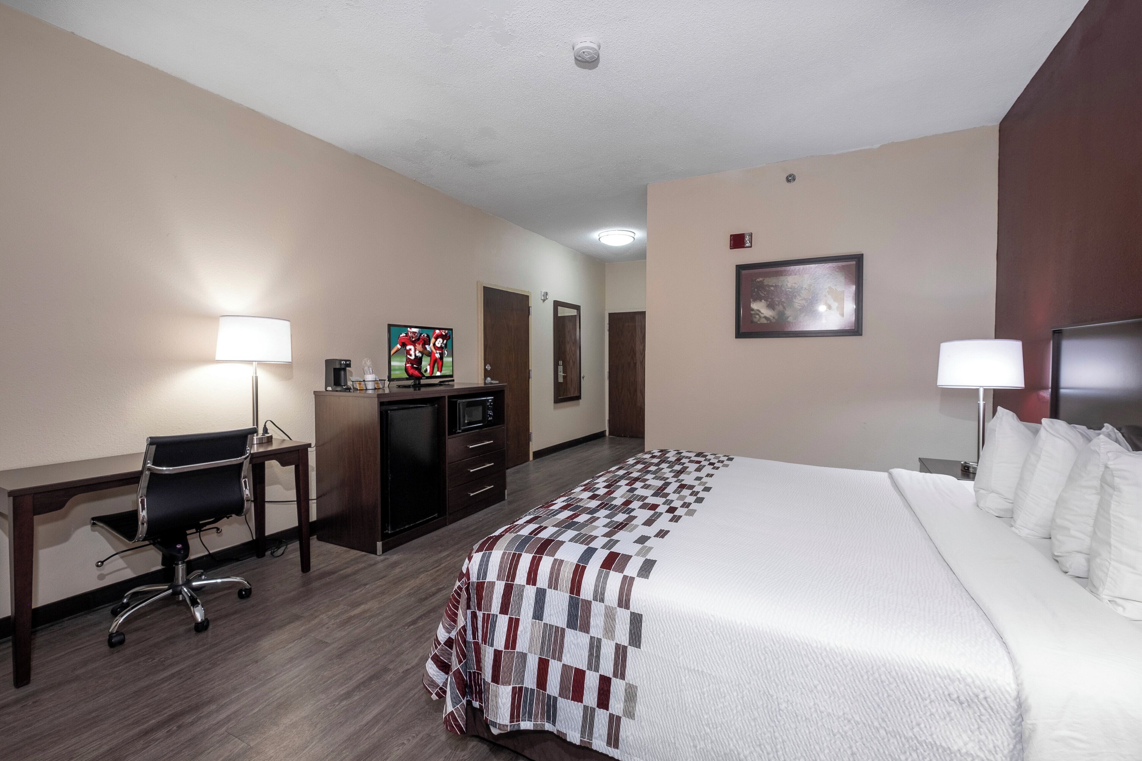 A hotel room with a bed, desk, chair, and a small kitchenette.