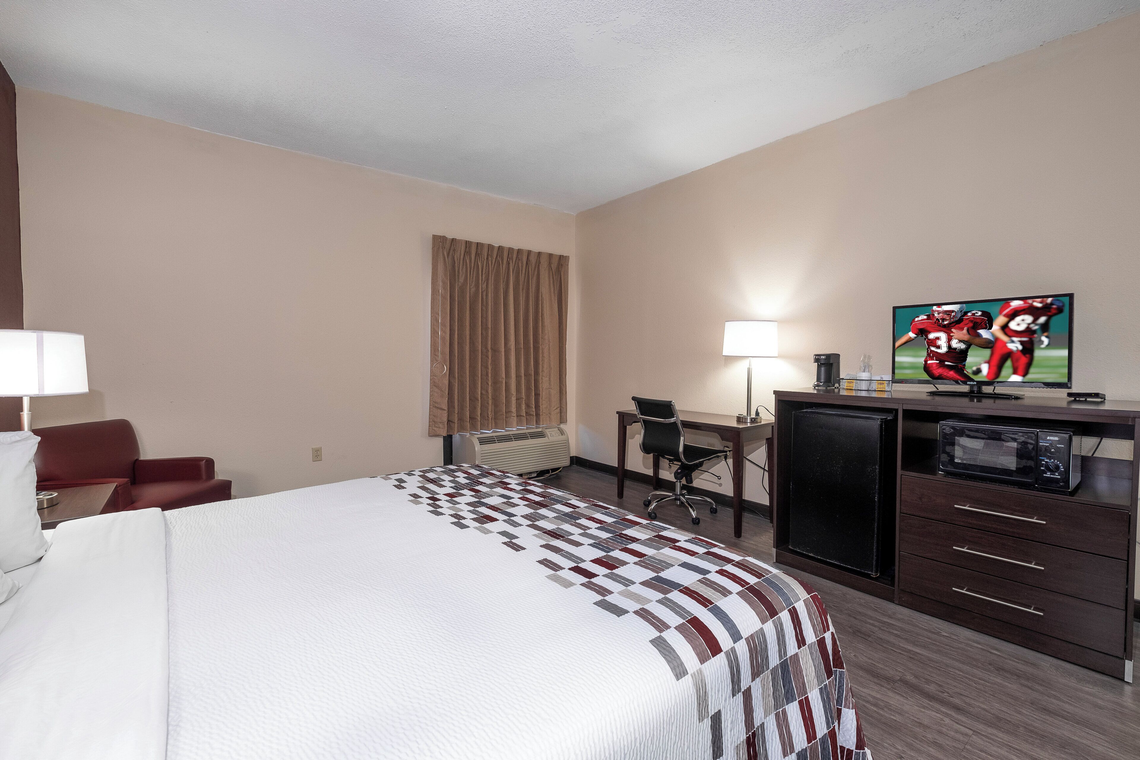 Habitación de hotel con cama, escritorio, silla, televisor y minibar.