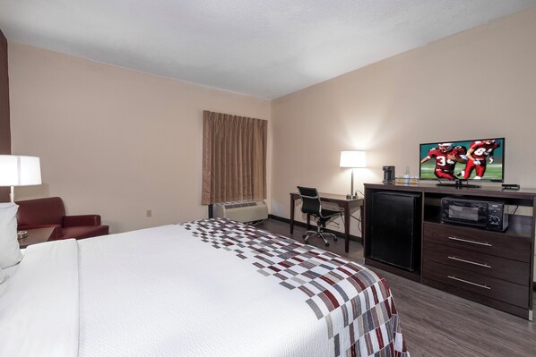 A hotel room with a bed, desk, chair, television, and a minibar.