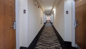 Un pasillo de hotel con pisos alfombrados, puertas de madera y carteles con números de habitación.