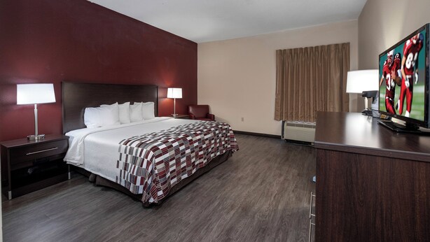 Habitación de hotel con cama, dos mesitas de noche, un escritorio, una silla, televisor y ventana con cortinas.
