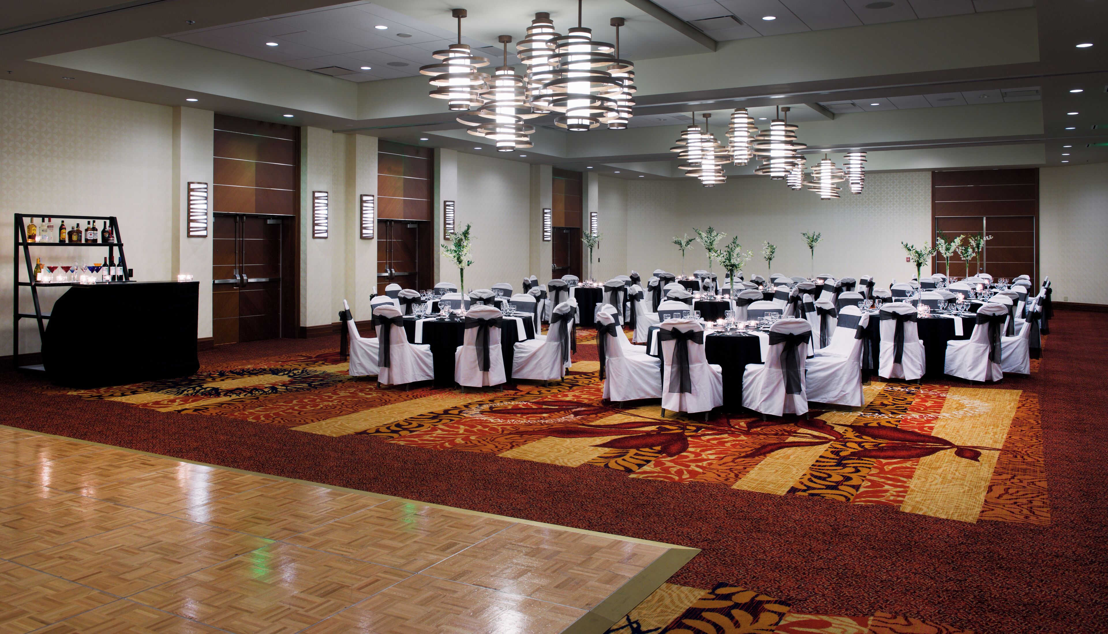 A banquet hall with round tables set for a formal event, featuring a carpeted floor and modern lighting fixtures.