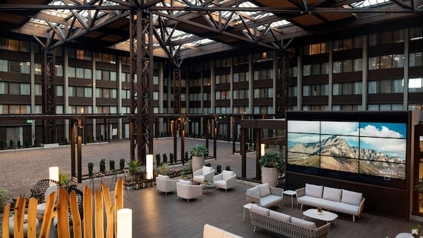 A spacious lobby with multiple seating areas, a large wall-mounted TV, and a view of a mountainous landscape. - Seattle Airport Marriott (SeaTac)