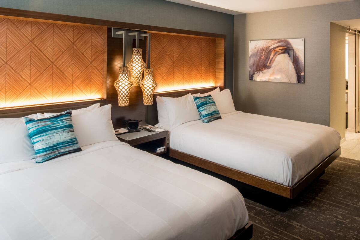 A hotel room with two beds, a nightstand, a lamp, and a painting on the wall.
