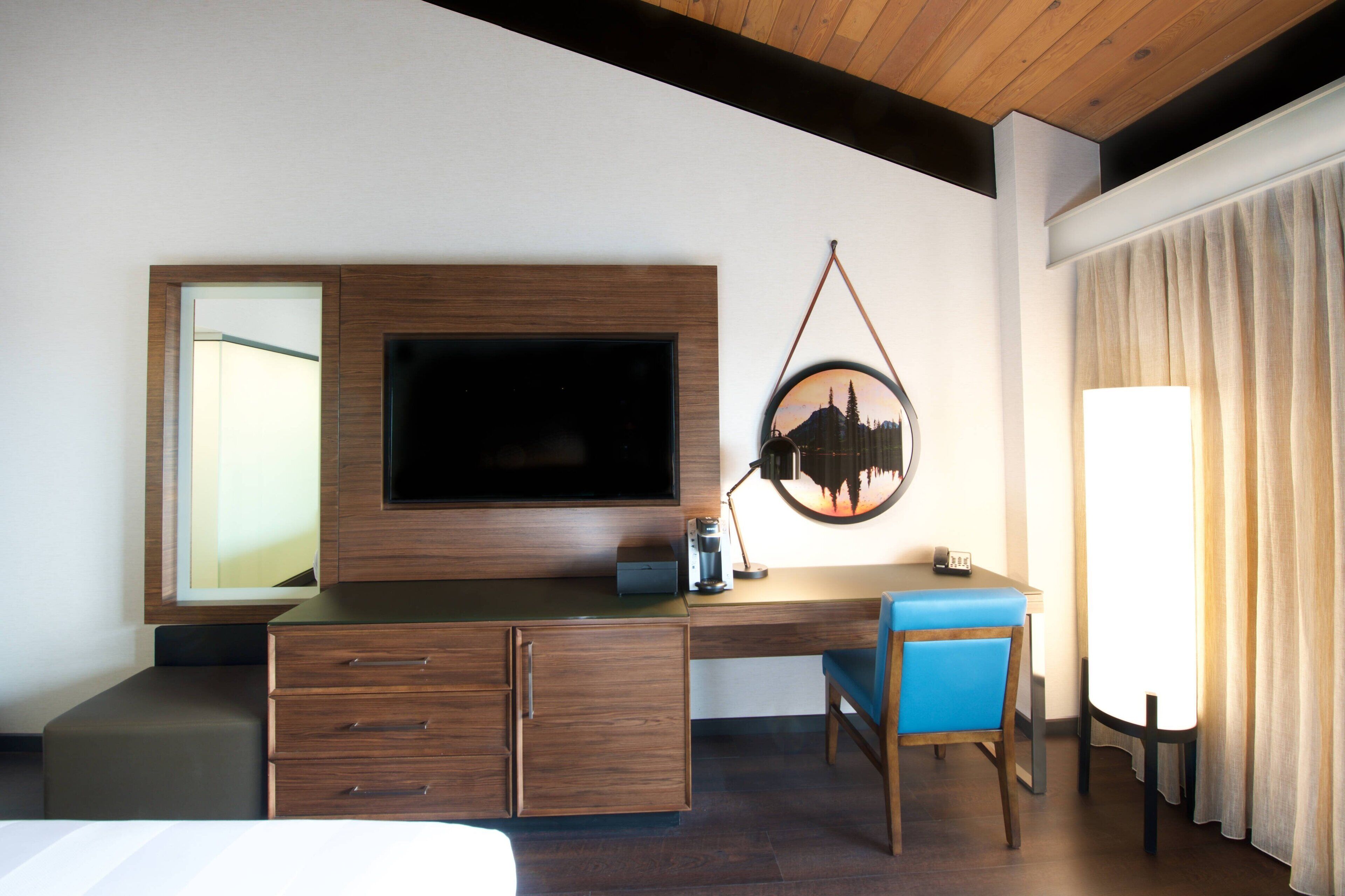 Habitación de hotel con un escritorio de madera, televisor de pantalla plana, cafetera y una silla.