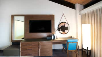 Habitación de hotel con un escritorio de madera, televisor de pantalla plana, cafetera y una silla.