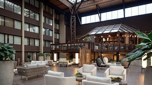 A spacious lobby with high ceilings, large windows, and a variety of seating arrangements including sofas and chairs. - Seattle Airport Marriott (SeaTac)