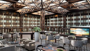 A spacious outdoor seating area with multiple tables and chairs, surrounded by bookshelves and a large plant. - Seattle Airport Marriott (SeaTac)