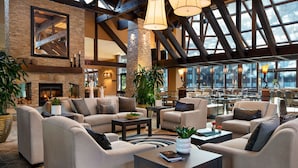 A spacious lobby with high ceilings, exposed beams, and large windows. There are multiple seating areas with sofas and tables, and a fireplace is visible in the background. - Seattle Airport Marriott (SeaTac)