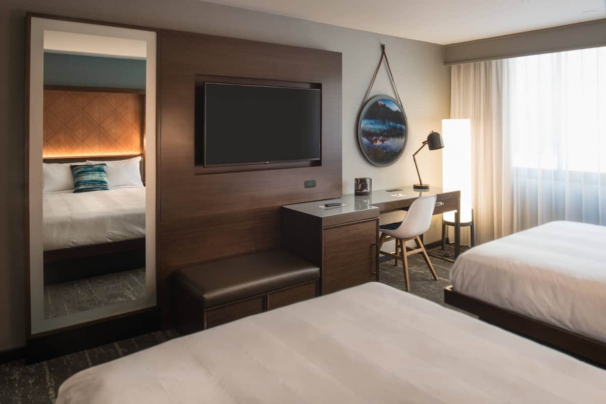 A hotel room with a bed, a desk, a chair, a TV, and a large window.