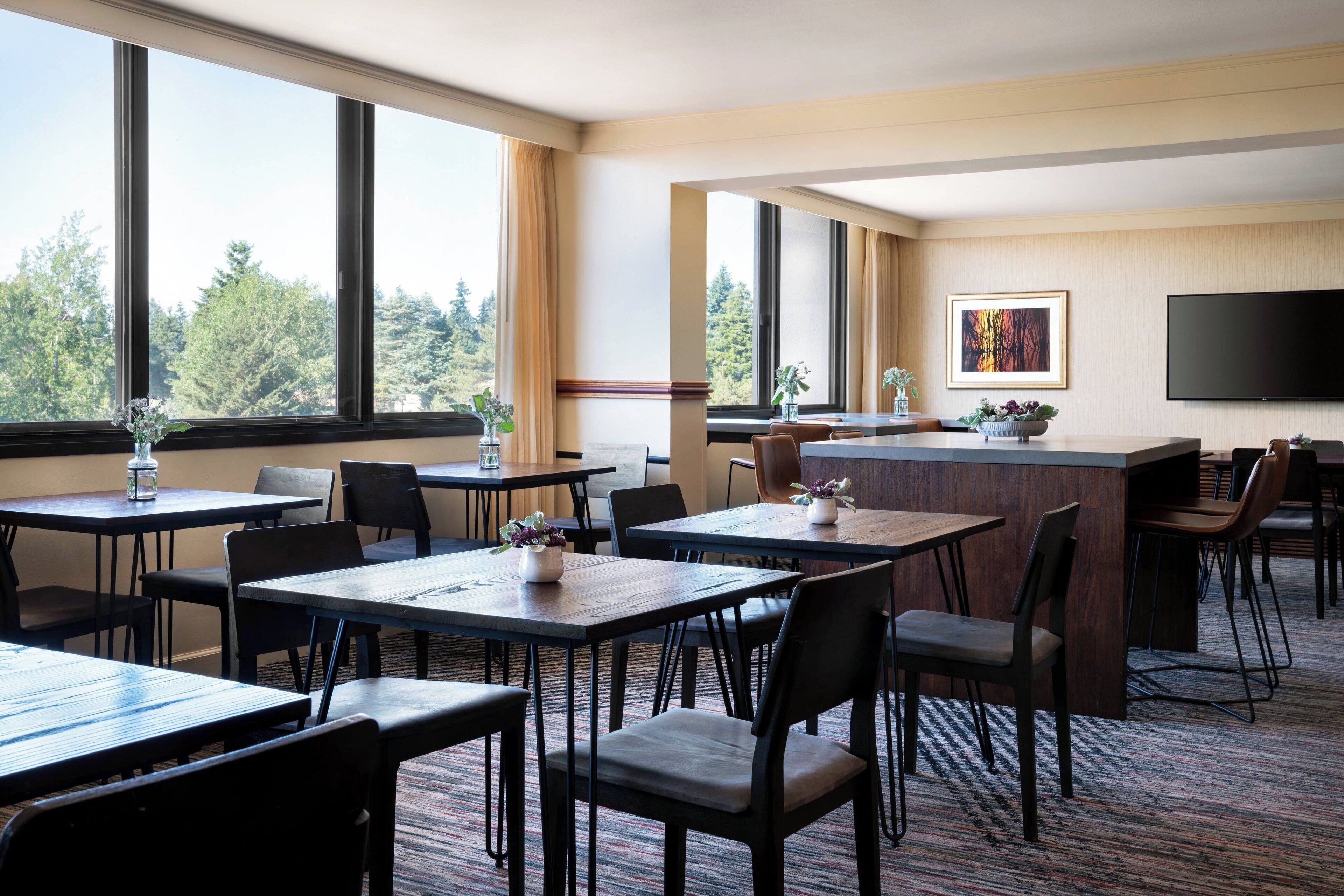 A hotel lobby with multiple tables and chairs, a reception desk, and a large TV on the wall.