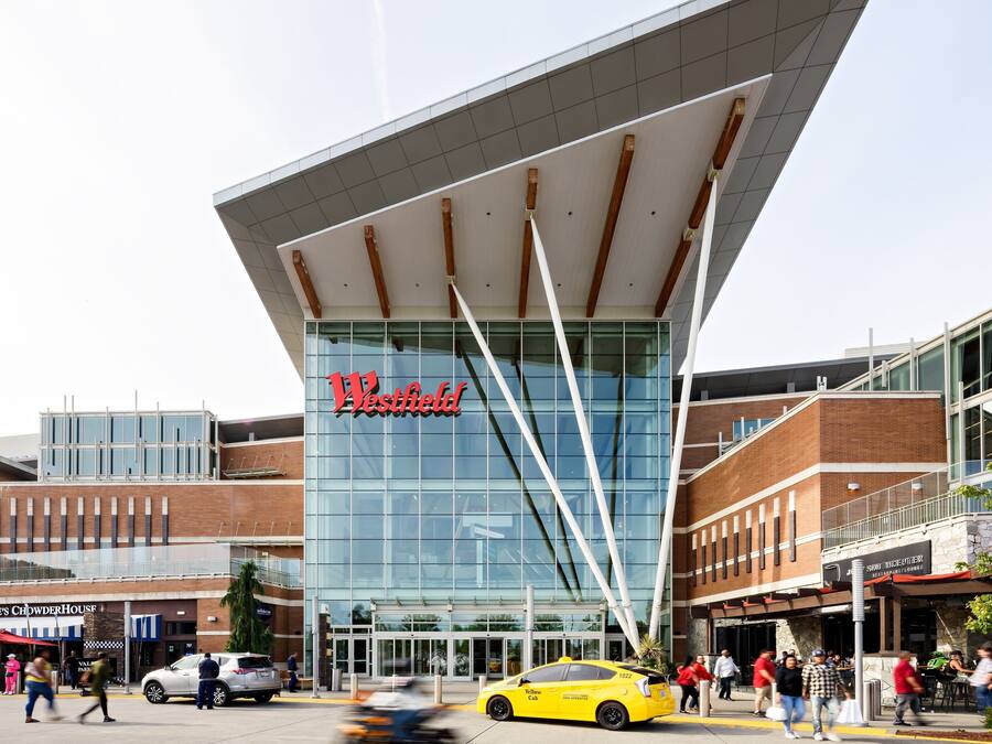 A modern building with a prominent 'Westfield' sign, featuring a glass facade and a unique architectural design with a sloped roof.