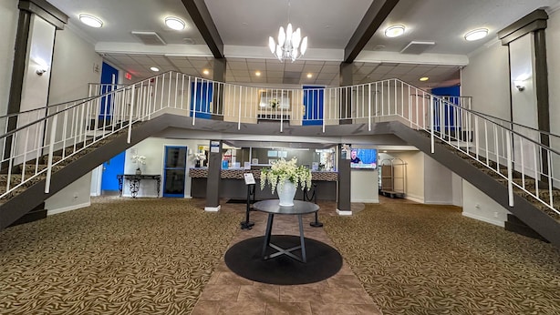 A spacious lobby with a central seating area, a reception desk, and a staircase leading to an upper level. - Motel 6 Rochester, NY - Airport (Rochester)