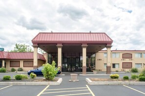 A hotel with a red roof, a covered entrance, and a parking lot with marked spaces.