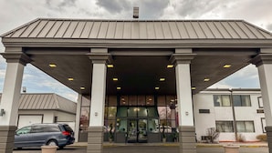 A building with a covered entrance, columns, and a parking lot. - Motel 6 Rochester, NY - Airport (Rochester)