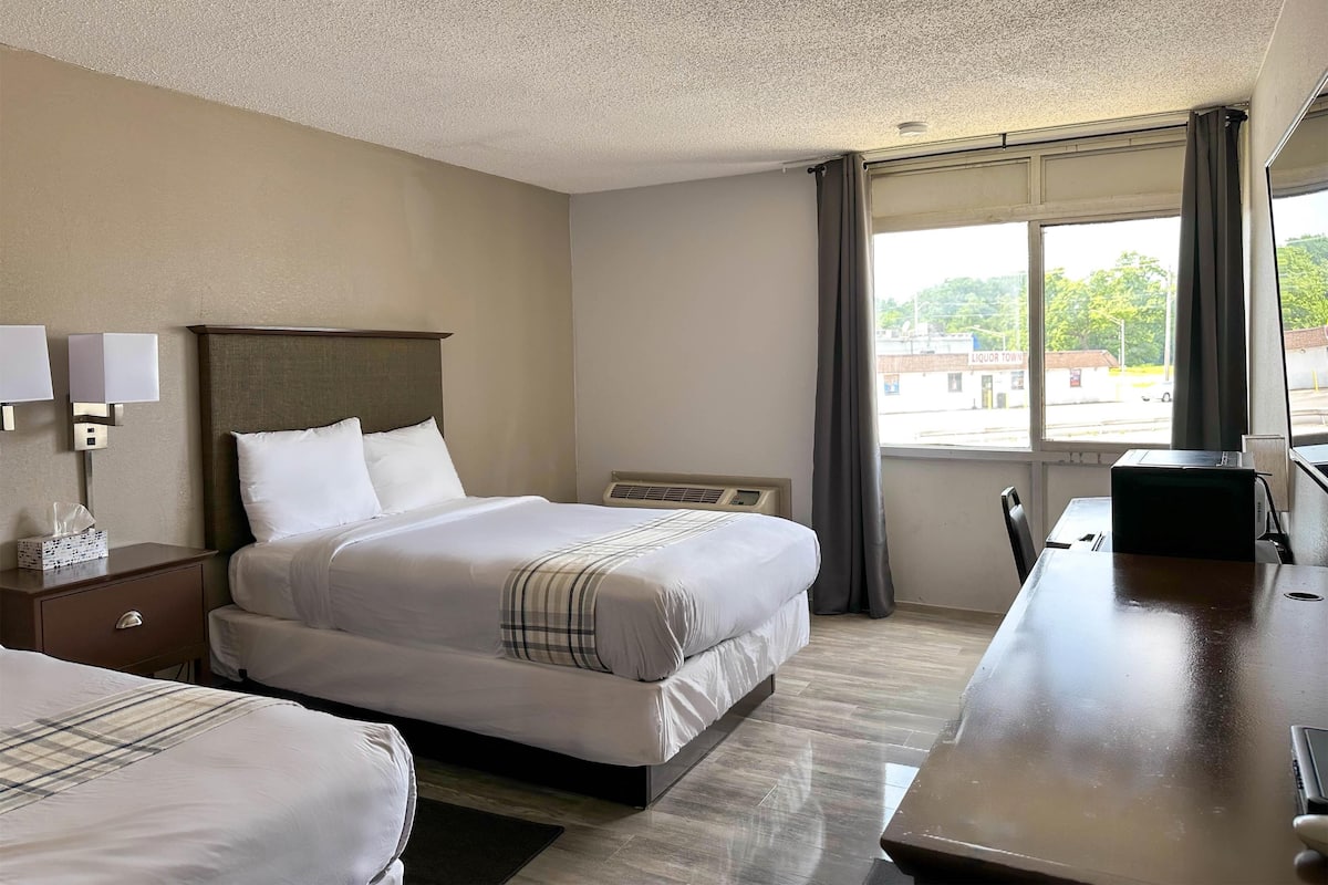 A hotel room with a bed, bedside table, lamp, and a window with curtains.