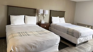 A hotel room with two beds, each with white linens and a plaid blanket. There are two bedside tables with lamps and a tissue box. The room has a neutral color scheme with beige walls and a wooden headboard. - Motel 6 Rochester, NY - Airport (Rochester)