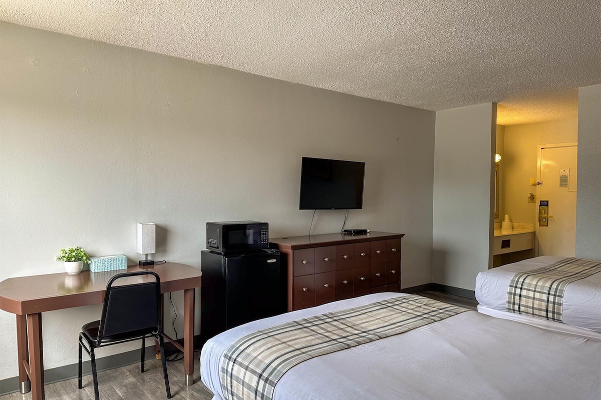 A hotel room with a desk, a television, a dresser, and two beds.
