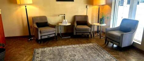 Un hall d’hôtel avec deux fauteuils, un canapé, un tapis, des lampes et un tableau encadré au mur.